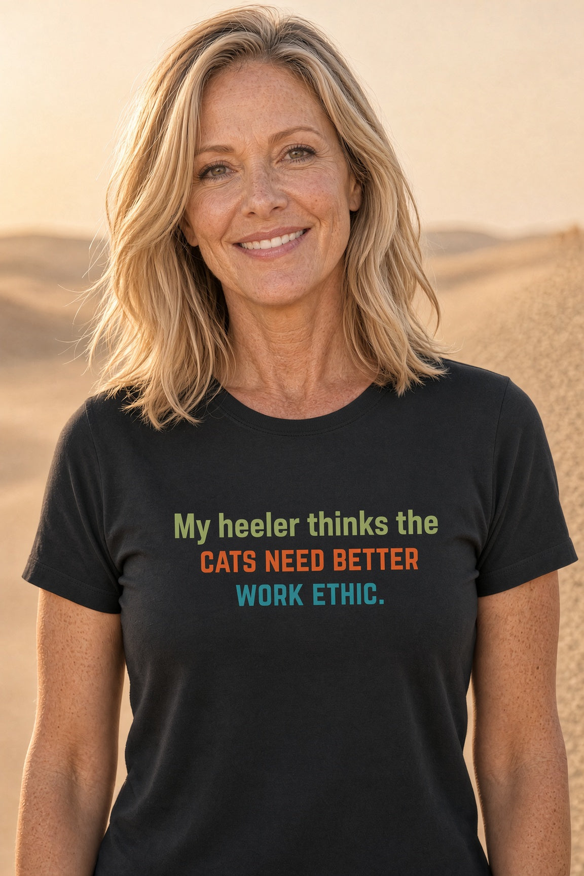 Woman smiling while wearing a black t-shirt with the text 'My heeler thinks the cats need better work ethic.'