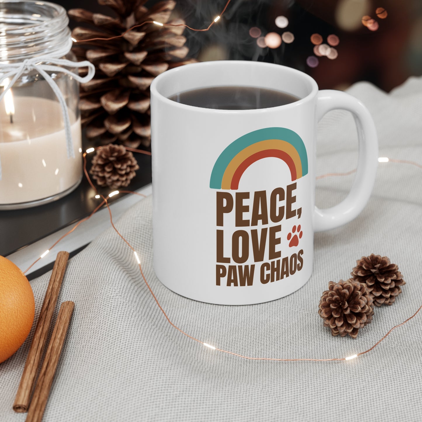 White mug with 'Peace, Love, Paw, Chaos' design on a table with decorative items.