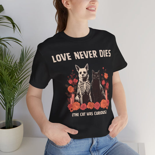 Person wearing a black t-shirt with skeleton dog, black cat, red flowers, and text reading Love Never Dies The Cat Was Curious