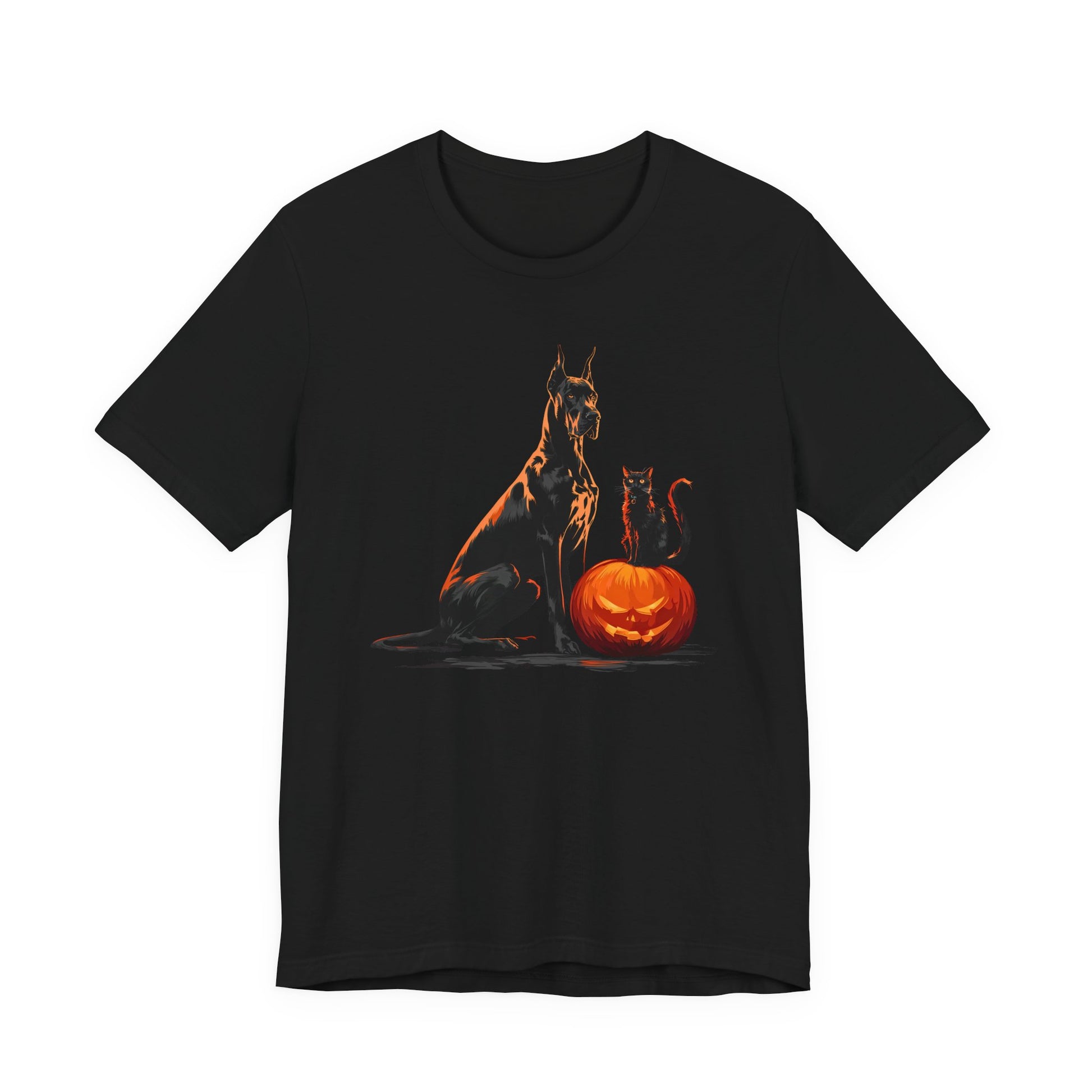 A black short-sleeve crewneck t-shirt featuring a graphic print of a black dog and a black cat sitting with a glowing orange jack-o'-lantern pumpkin, shown against a plain white background.