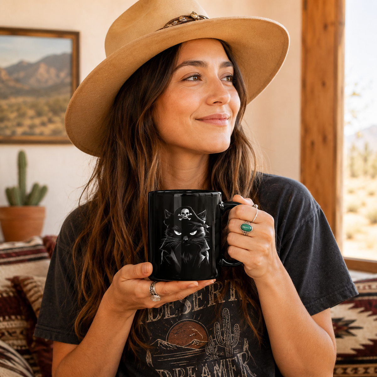 Woman holding a black mug with a pirate cat design, smiling in a desert-themed interior.