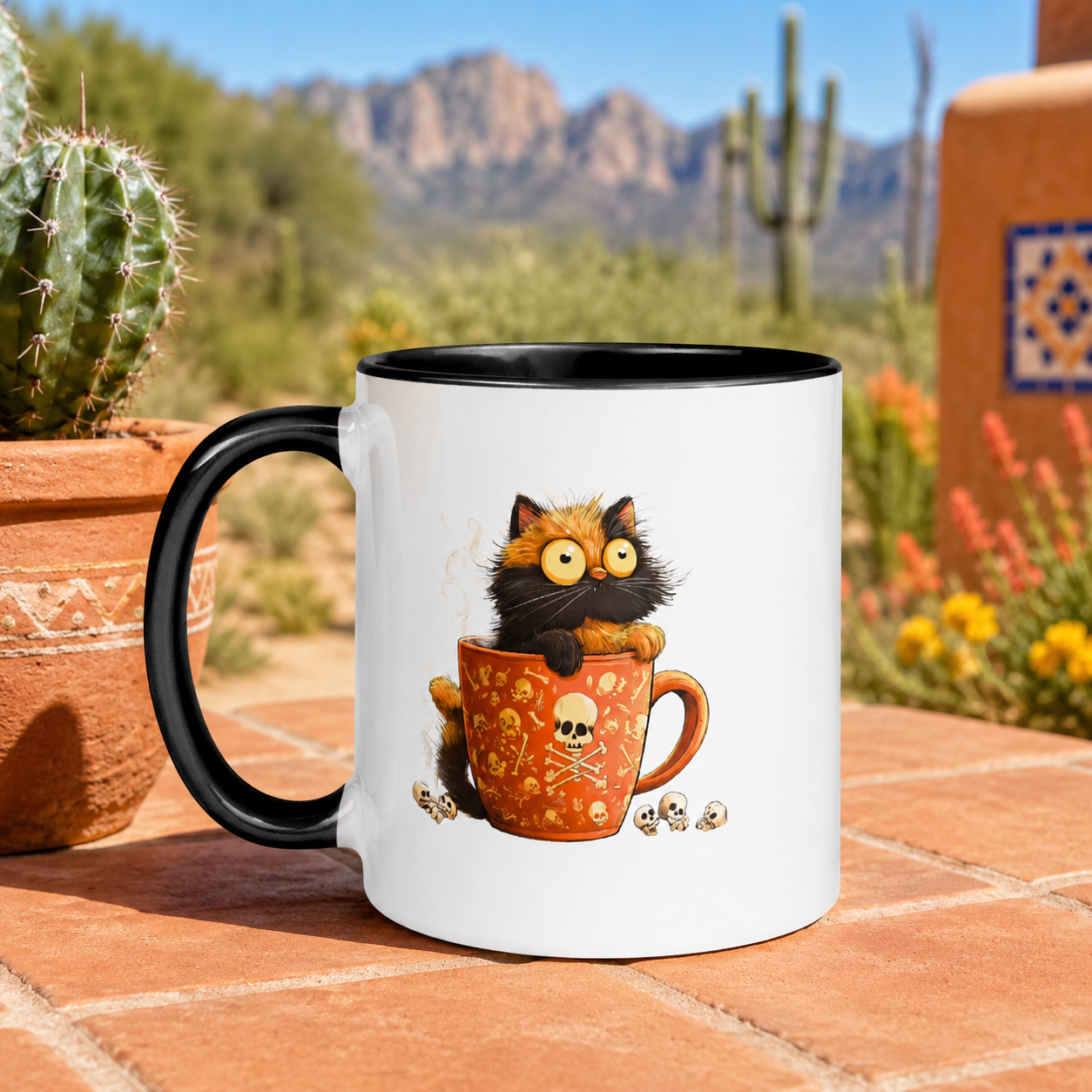 A white ceramic coffee mug with a black handle and black interior, featuring a cartoon black and orange cat peeking out of an orange mug with skull and crossbones details. The mug is placed on a terracotta tile surface with a blurred desert garden and mountains in the background.
Digitally created lifestyle mockup