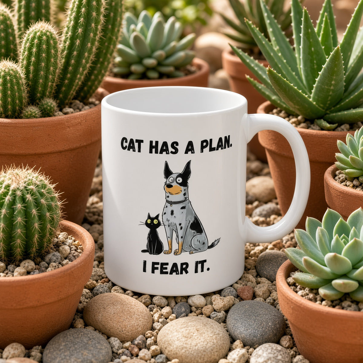 White mug featuring a dog and cat with the text 'CAT HAS A PLAN. I FEAR IT.' surrounded by cacti.