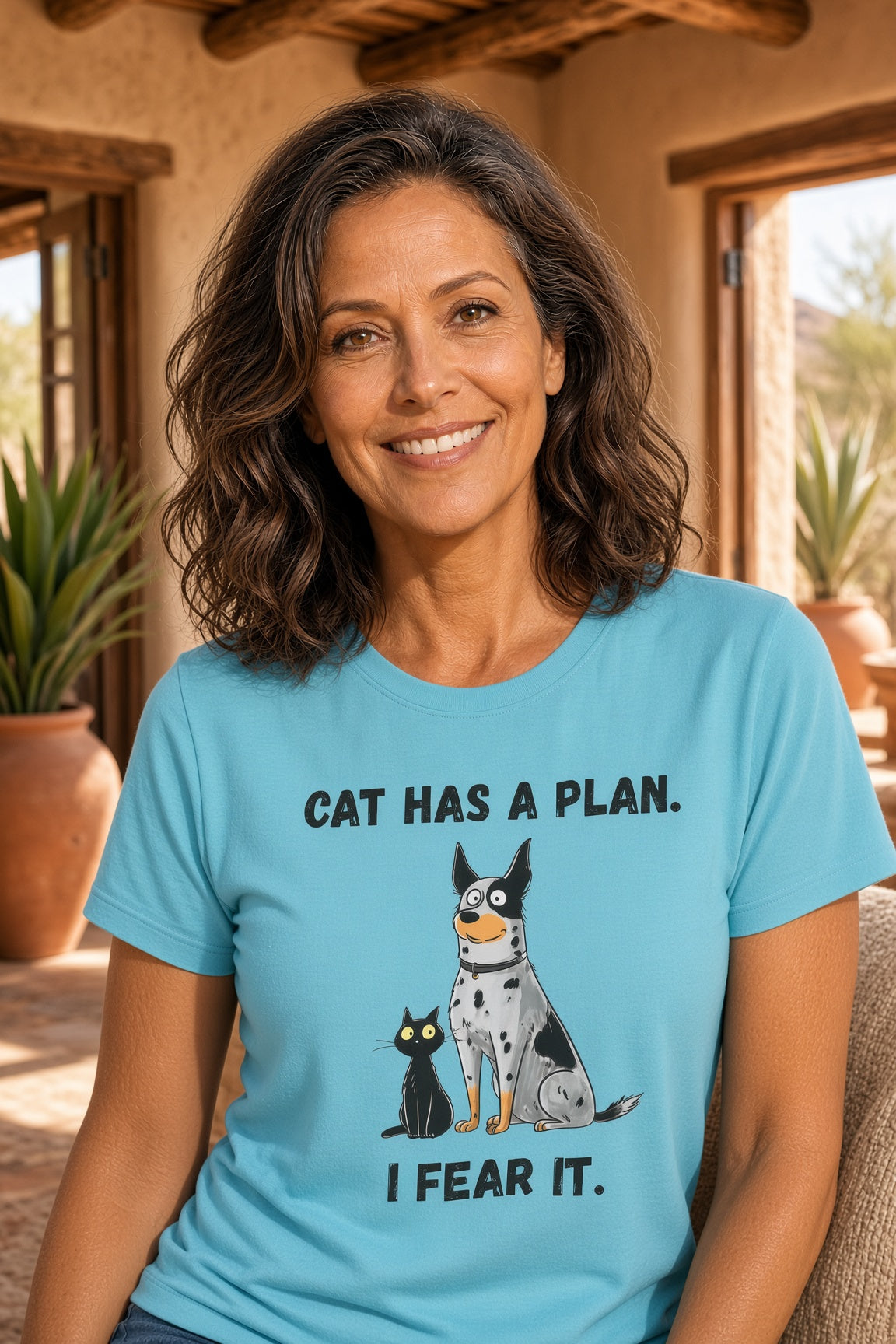 Woman wearing a blue tee with a cartoon dog and cat design, text reads 'CAT HAS A PLAN. I FEAR IT.'