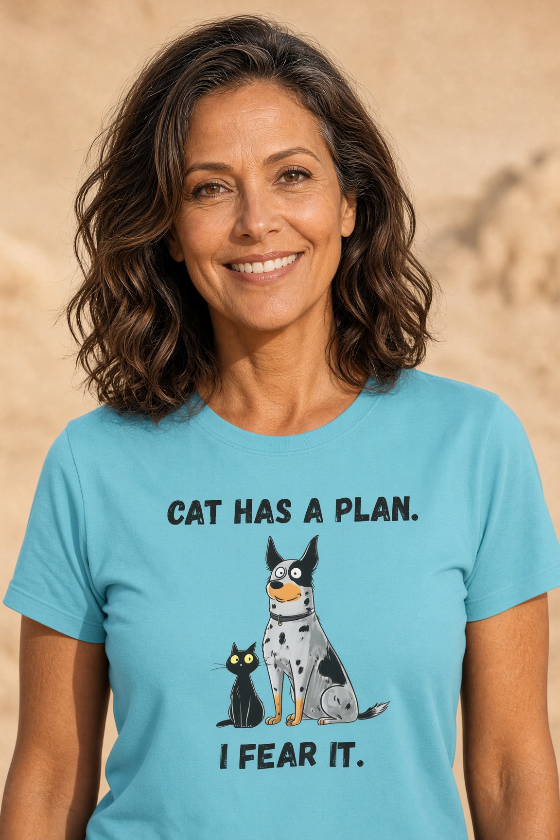 Woman smiling in a blue t-shirt featuring a blue heeler and black cat design, text reads 'CAT HAS A PLAN. I FEAR IT.'