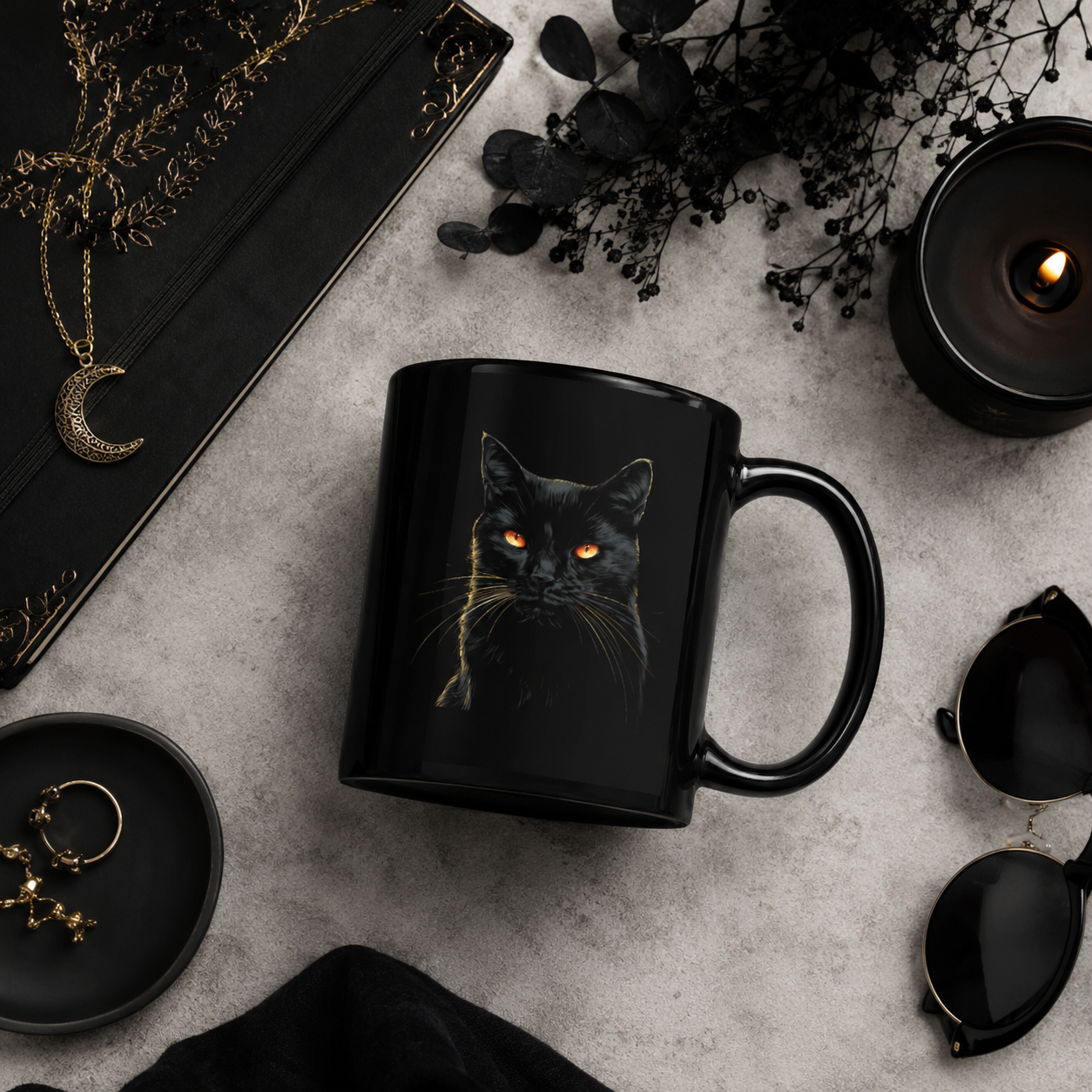 Black cat mug with glowing orange eyes in a moody flat lay with candle, notebook, and dark accessories.