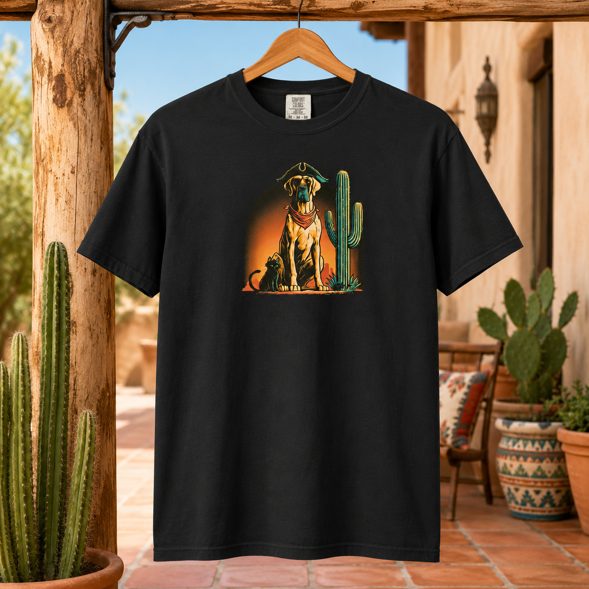 Black t-shirt with a dog and cactus design hanging on a wooden beam in a desert setting.