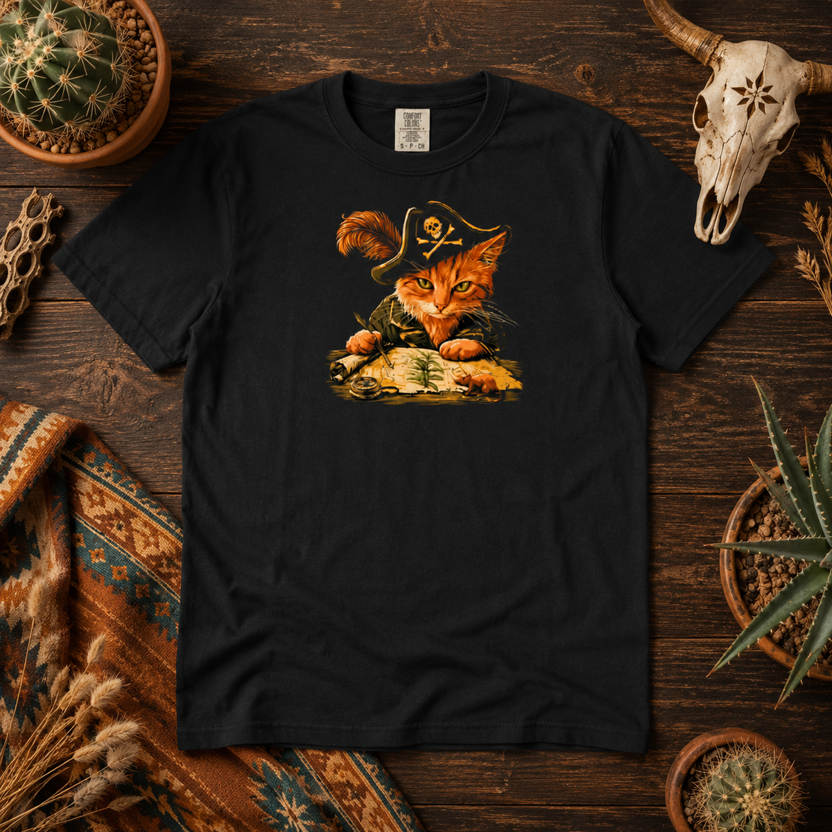 Black t-shirt with a pirate cat design displayed on a wooden surface with cacti.