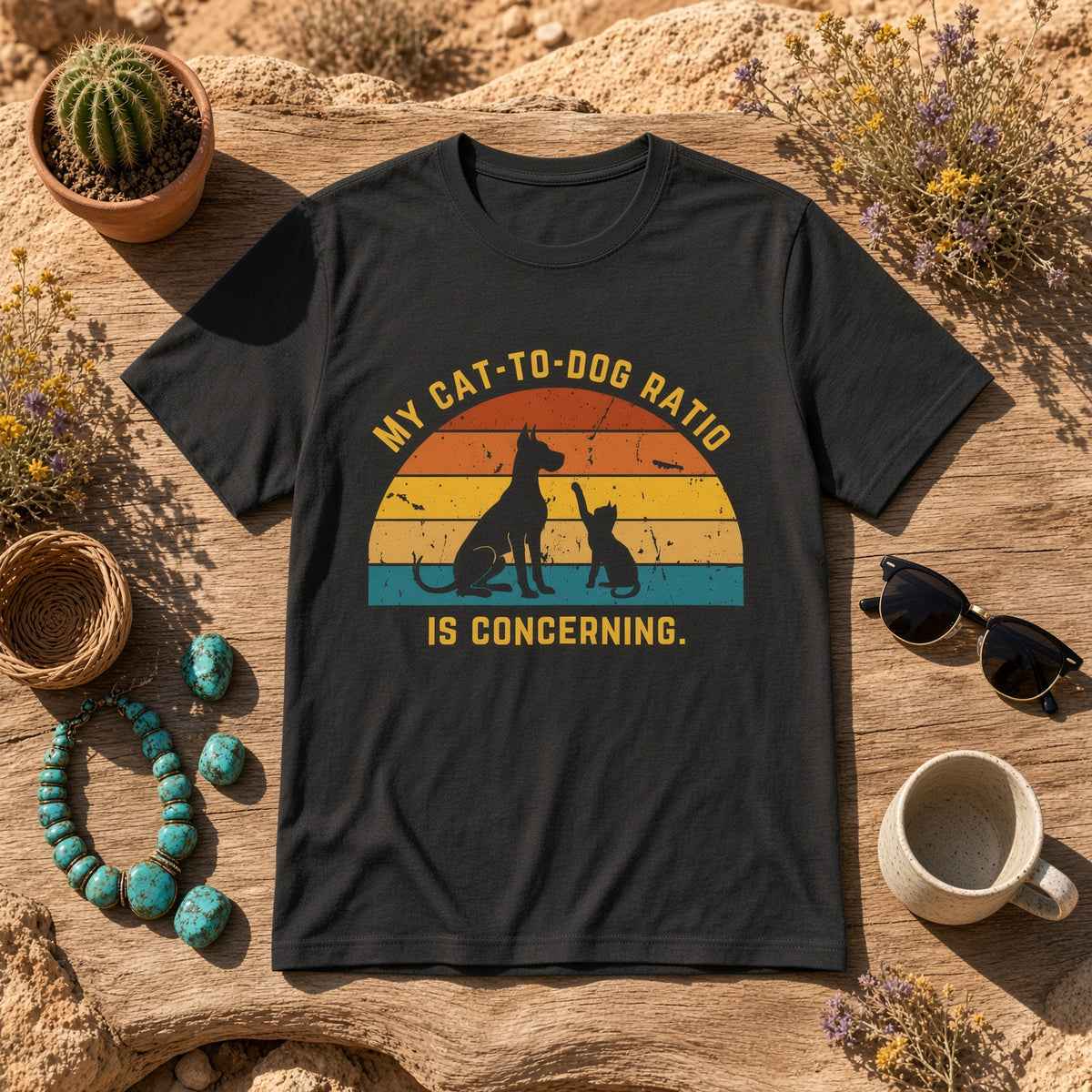 Black t-shirt with a retro design of a cat and dog on a rustic table surrounded by accessories and the text 'My Cat-to-Dog Ratio Is Concerning.'