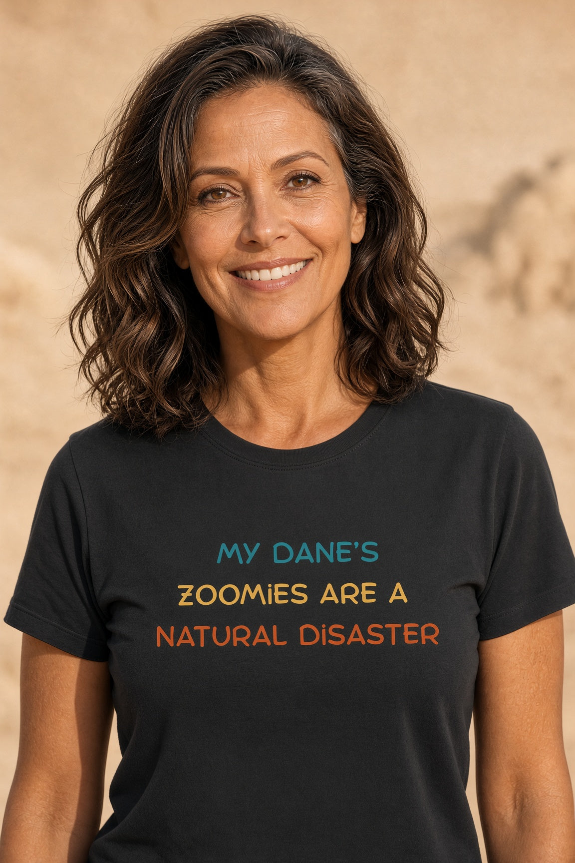Woman smiling while wearing a black t-shirt with colorful text saying 'My Dane’s Zoomies Are A Natural Disaster'.