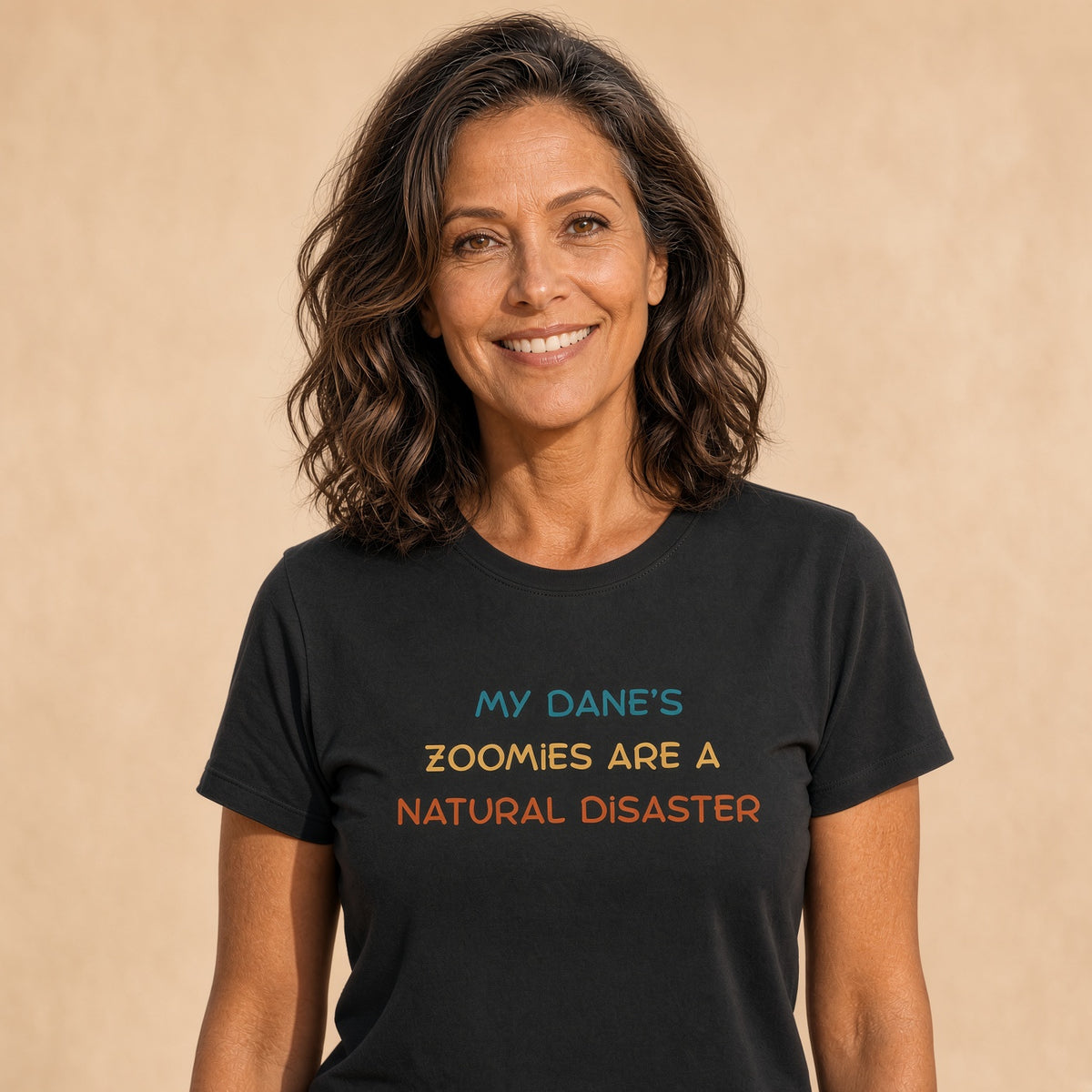 Woman smiling while wearing a black t-shirt with colorful text design with colorful text saying 'My Dane’s Zoomies Are A Natural Disaster'.