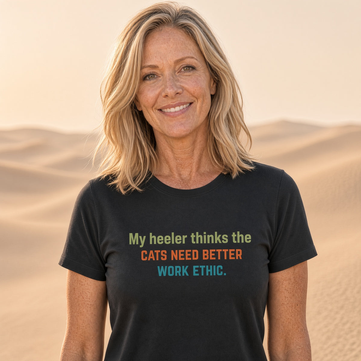 Woman smiling in a black t-shirt with the text 'My heeler thinks the cats need better work ethic.'