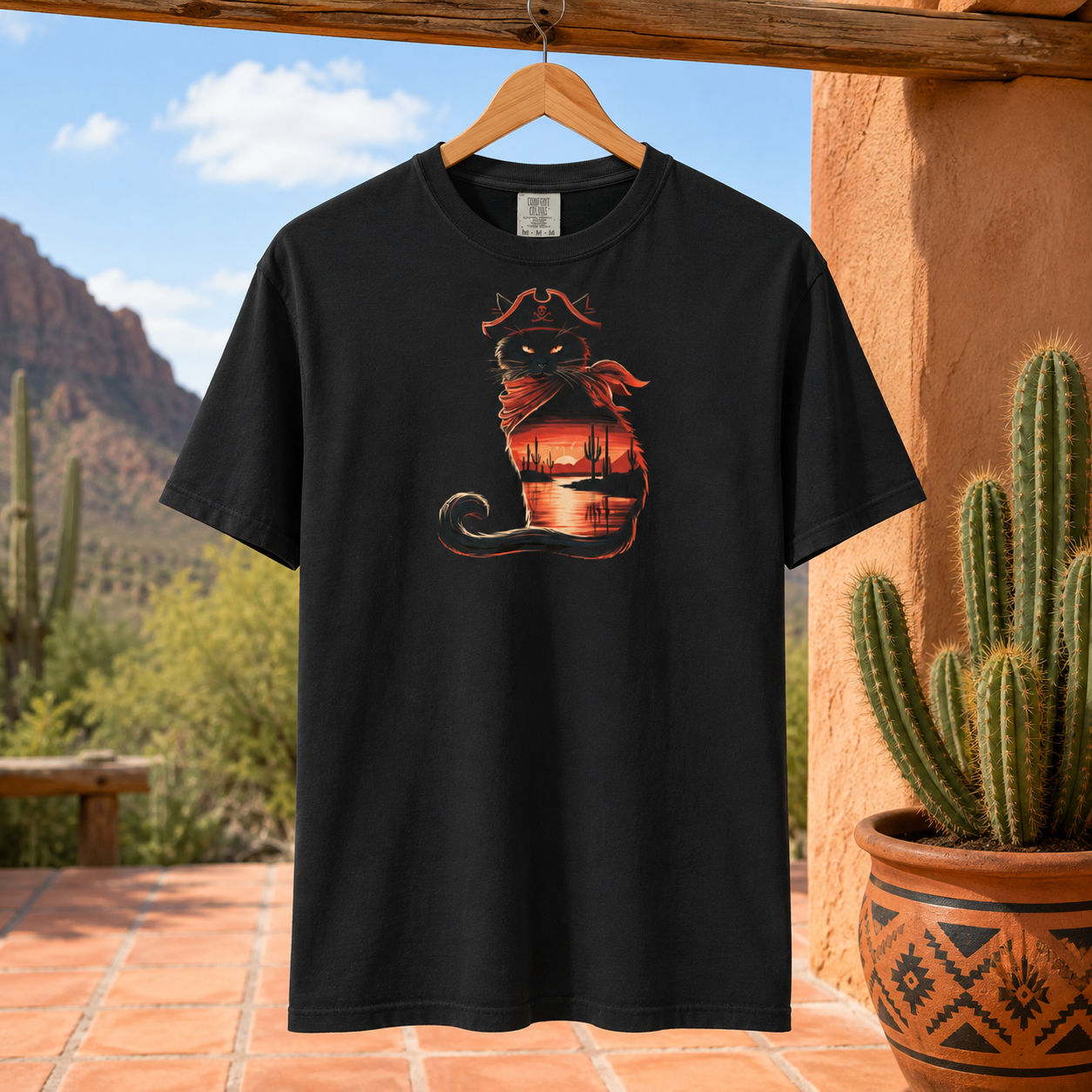 Black t-shirt with a pirate cat design hanging outdoors near cacti.