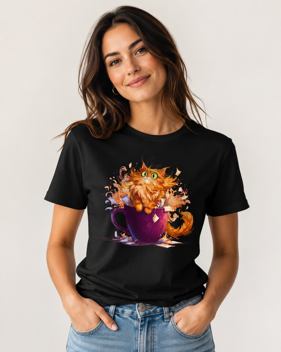 A woman wearing a black short-sleeve t-shirt with a colorful graphic of an orange cat popping out of a purple teacup, paired with blue jeans, against a light gray background.