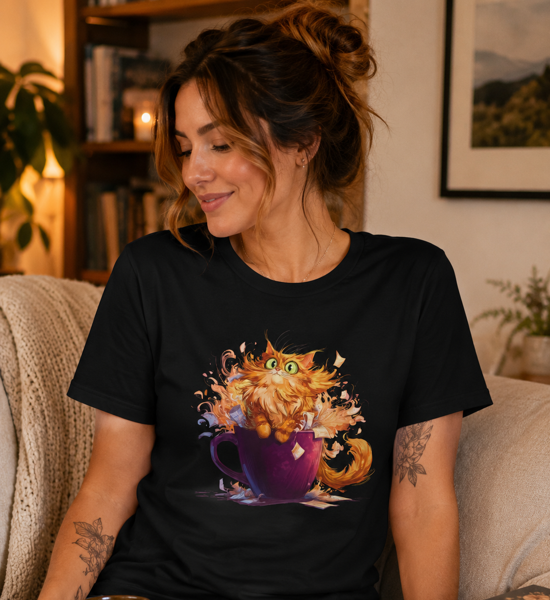 A woman sitting on a couch wearing a black graphic t-shirt with a colorful illustration of an orange cat jumping out of a purple mug. 