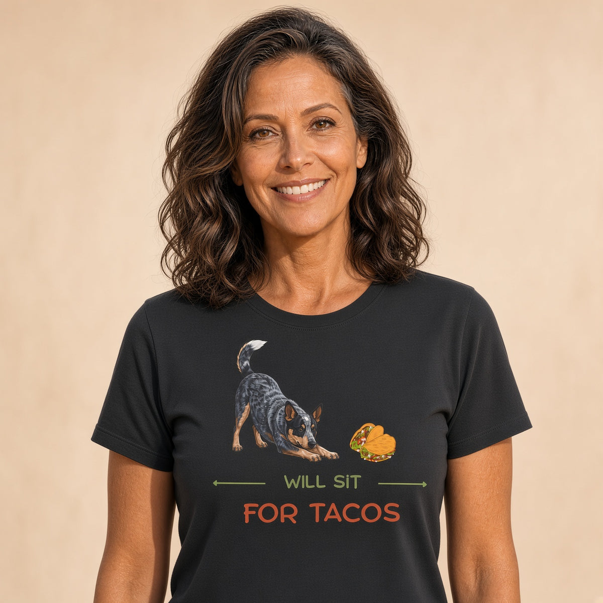 Woman smiling in a black t-shirt featuring a Blue Heeler and taco design with the text 'WILL SIT FOR TACOS'.