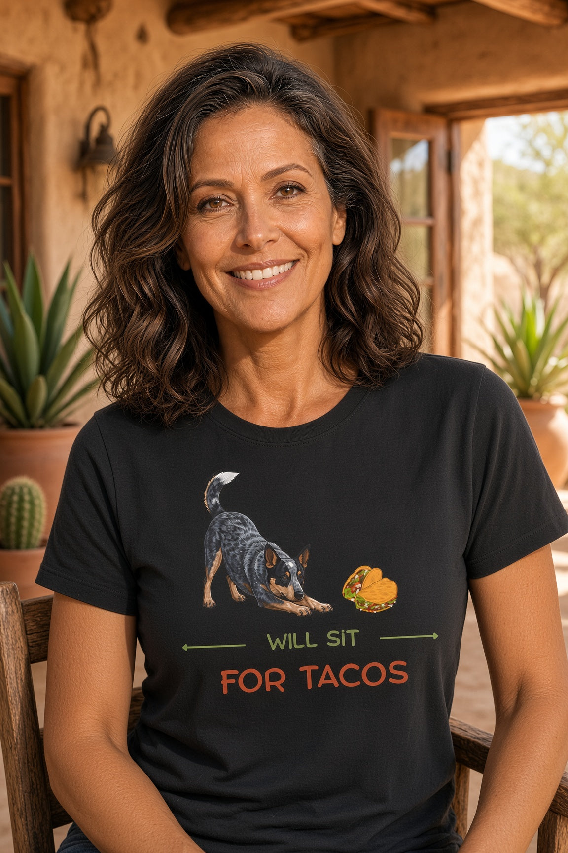 Woman smiling while wearing a black shirt with a Blue Heeler and taco design with the text 'WILL SIT FOR TACOS'.