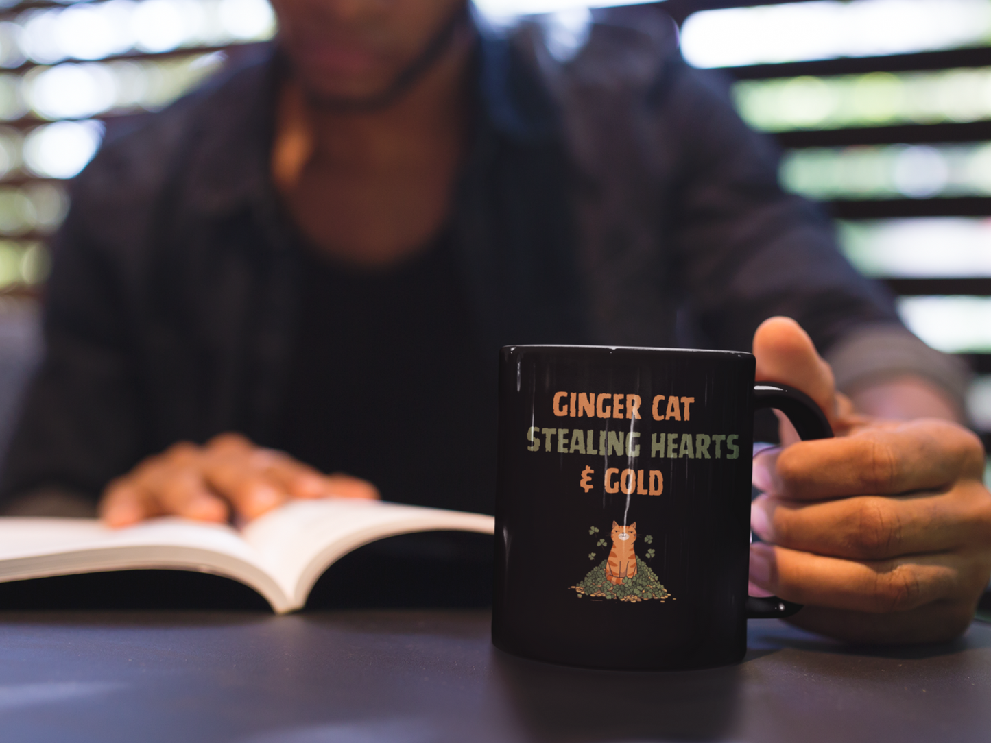 Black glossy mug with ‘Ginger Cat Stealing Hearts & Gold’ text and orange tabby sitting on shamrocks and coins.