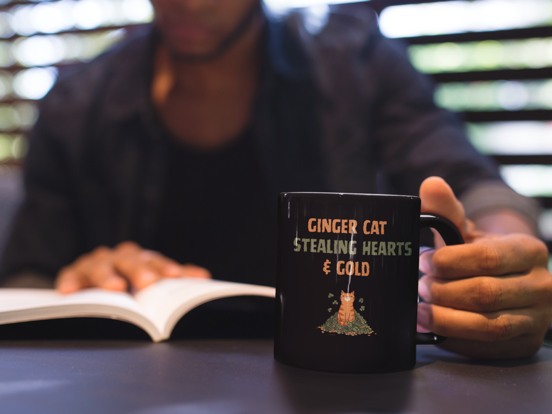 Black glossy mug with ‘Ginger Cat Stealing Hearts & Gold’ text and orange tabby sitting on shamrocks and coins.