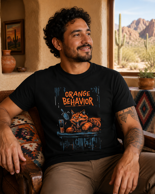 Man wearing a black Orange Behavior cat graphic t-shirt in a cozy Southwestern desert home with cactus views, rustic decor, and warm Arizona-inspired styling.