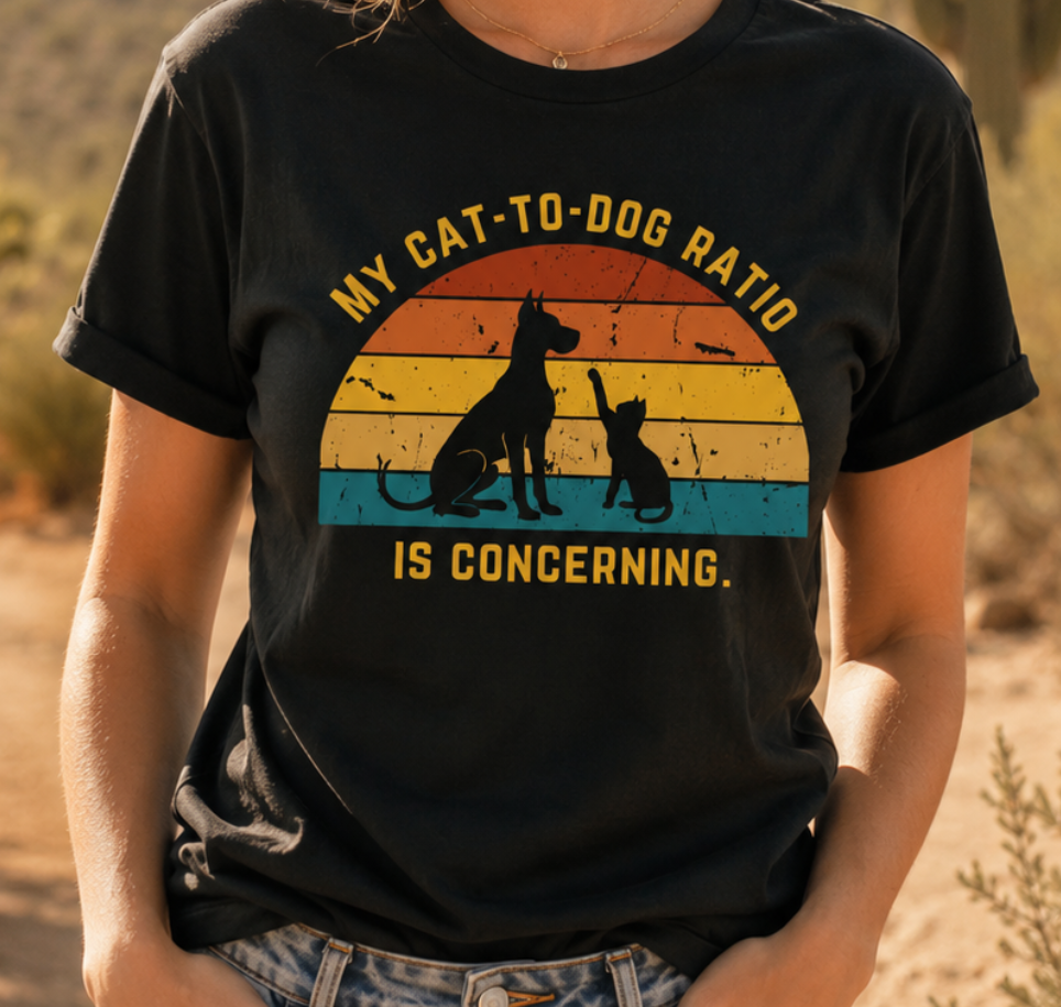 Woman wearing a black My Cat-to-Dog Ratio Is Concerning t-shirt in a cozy indoor setting, featuring a retro dog and cat graphic.