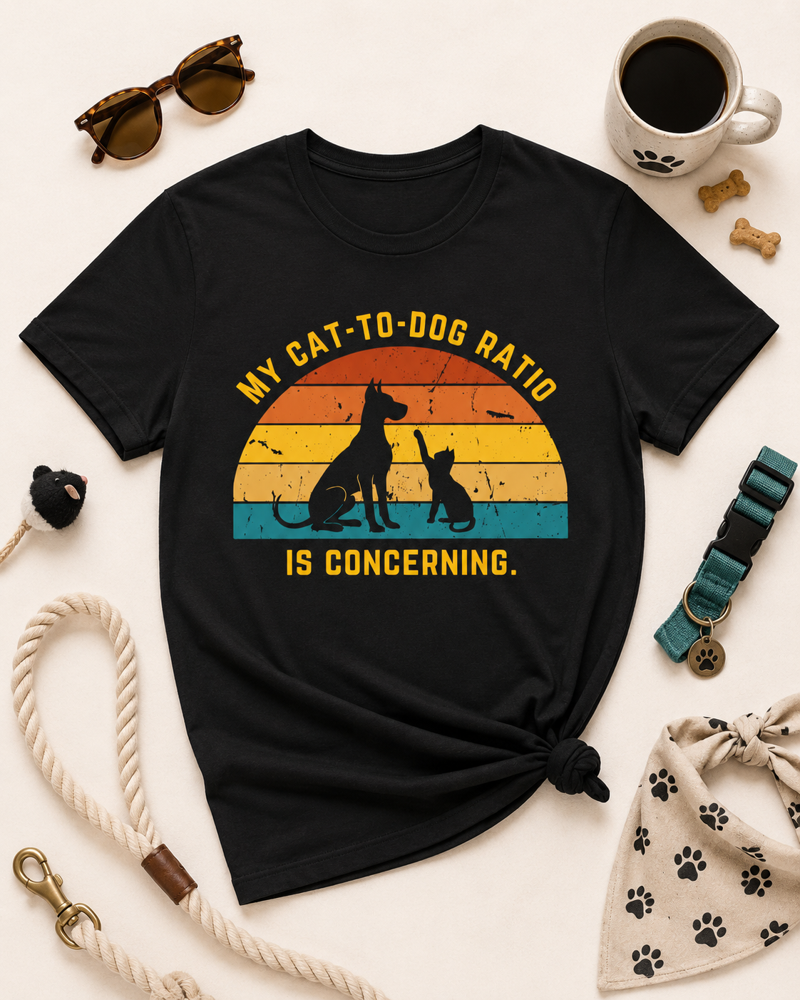 Black My Cat-to-Dog Ratio Is Concerning t-shirt styled in a flat lay with sunglasses, coffee mug, rope leash, collar, and paw print bandana.